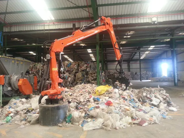 Bras de grue orange en activité dans une installation de recyclage